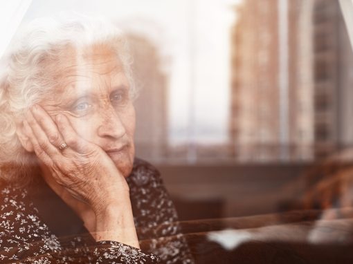 Elderly woman sitting alone and looking sadly outside the window
