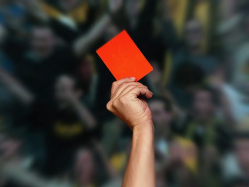 A hand holding a red card up in front of a blurred crowd